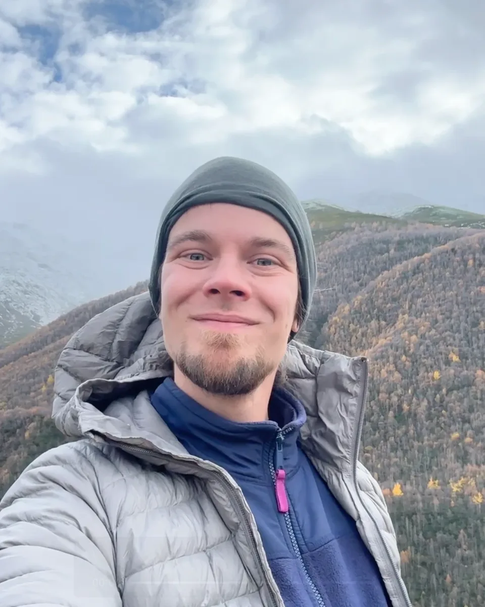Dmitrii lächelt auf einem Bergkamm über herbstlichem Wald bei Dilijan, Armenien