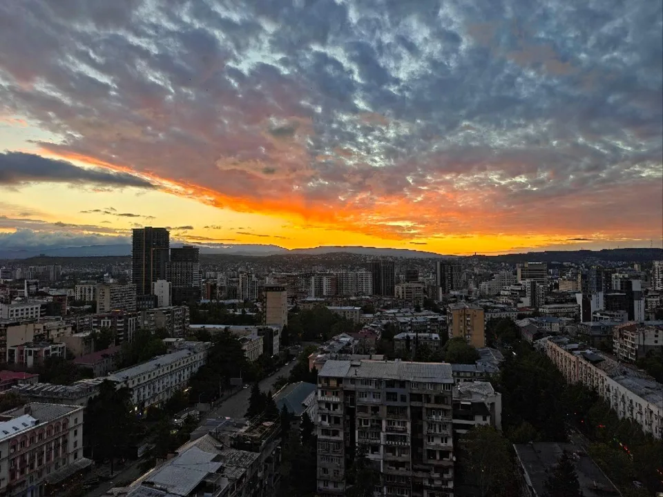 Phone photo of a city at sunset, orange sky under gray-blue clouds